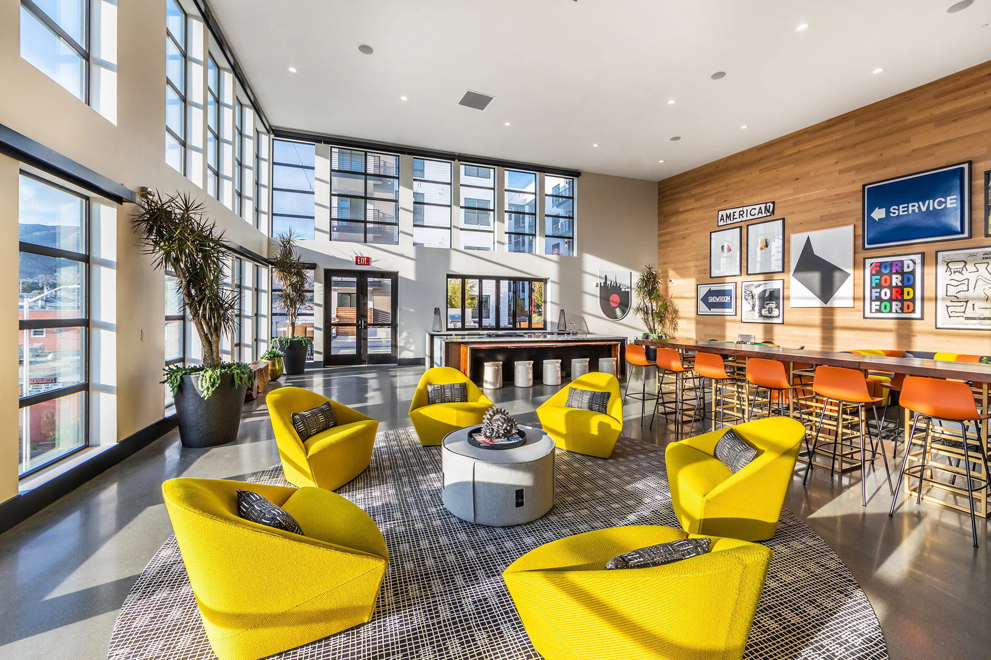 Evening shot of clubroom with a variety of plush and bar-style seating, retro artwork, and large windows.