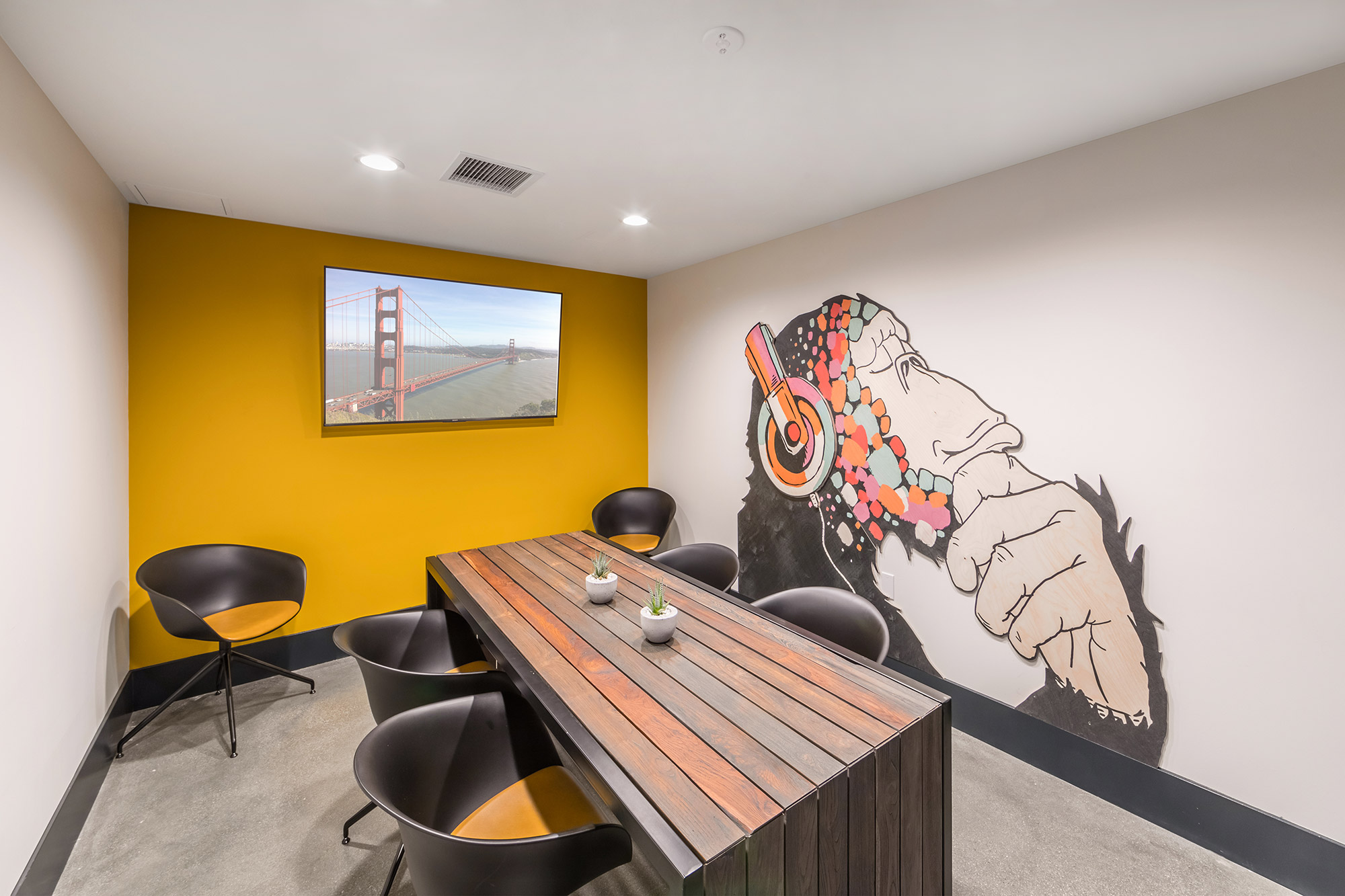 Private office with modern conference table, accent wall, bucket seats and a wall-mounted TV.