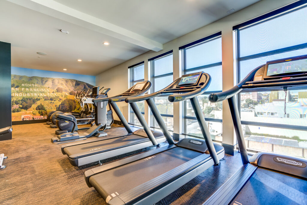 Fitness center with treadmills, accent wall, elliptical machines, and large windows with a view.