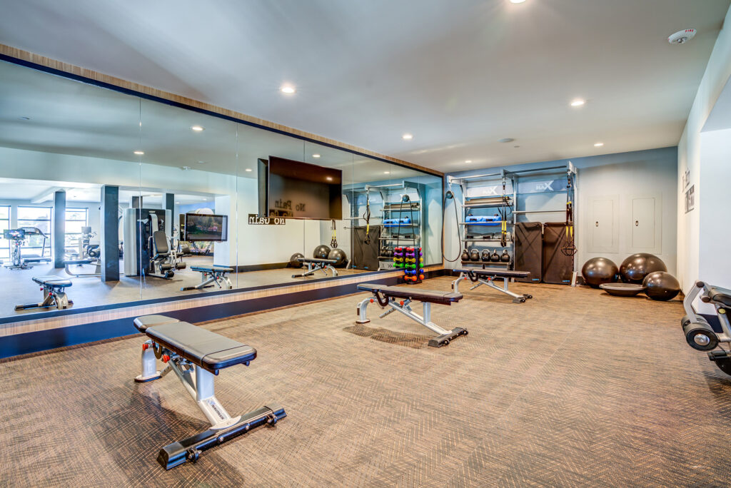 Fitness center room with flat screen TV, mirrored walls, benches, free weights, and medicine balls.