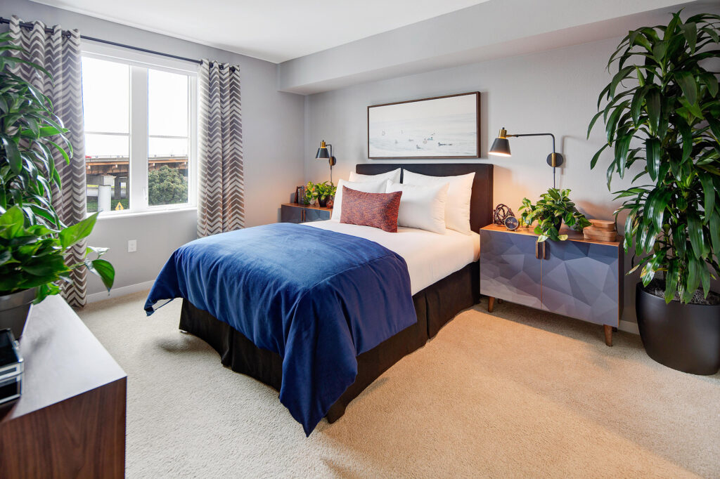 Bedroom with plush carpeting, large window, queen-sized bed, dresser and nightstands.