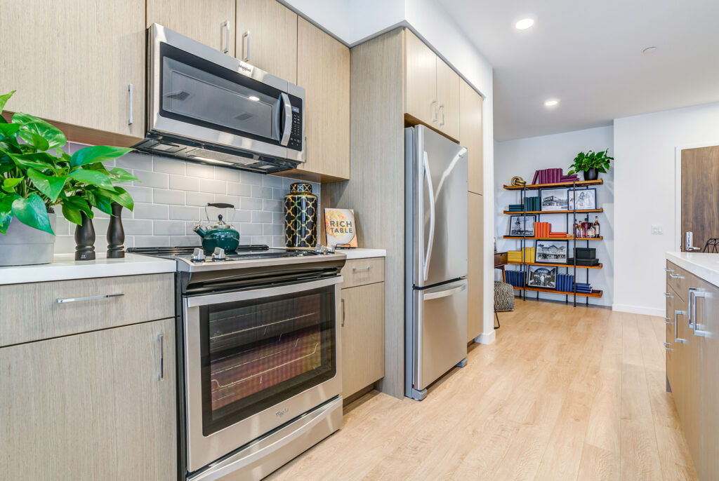 Kitchen with stainless steel appliances, quartz countertops, gray backsplash and wood-style flooring.