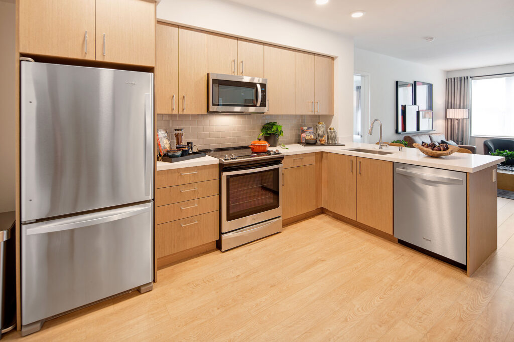 Kitchen with stainless steel Whirlpool appliances, quartz counters, gray backsplash, and wood-style floor that is open to the living room.