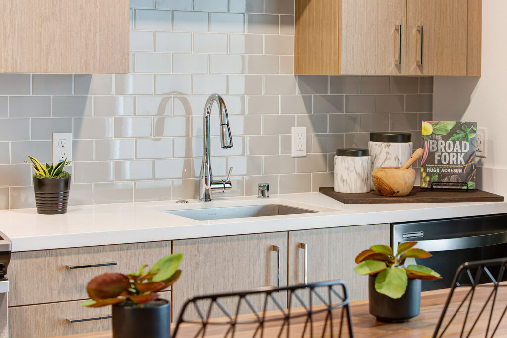 Kitchen detail of quartz counters, gray backsplash, and single basin Kohler stainless steel sink.