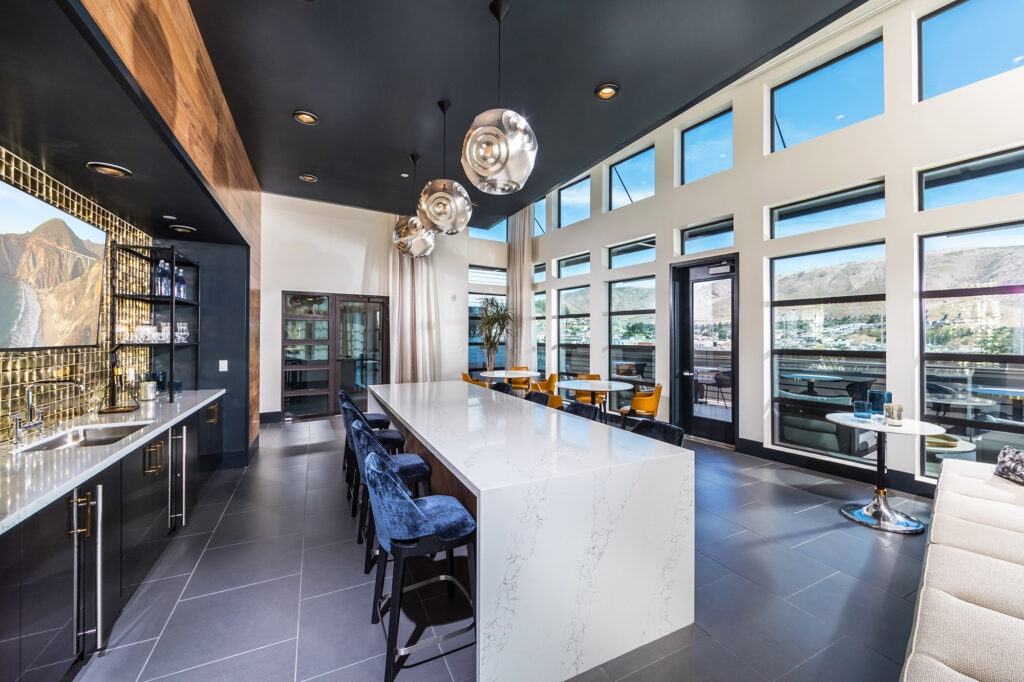 Clubhouse kitchen area with family-style seating, bistro-style seating, large wall-mounted TV and large windows overlooking the town.