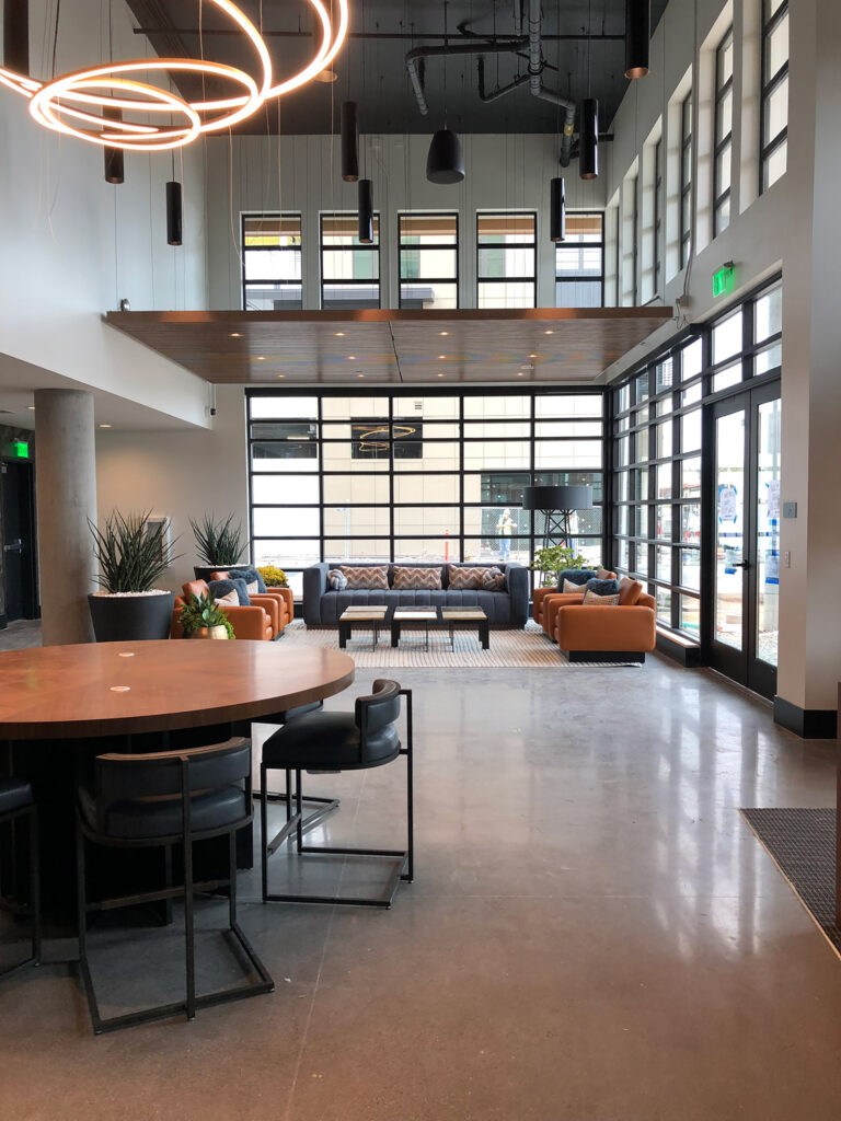 Clubhouse kitchen area with family-style seating, bistro-style seating, door leading to balcony seating with a view, and large wall-mounted TV.