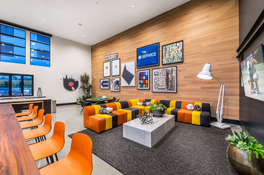 Clubroom with retro artwork, colorful furniture, wall-mounted flat-screen TV, and family-style bar seating.